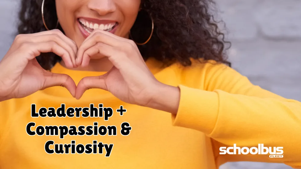A smiling person in a yellow sweater forms a heart shape with their hands above the words "Leadership + Compassion & Curiosity." The graphic accompanies a School Bus Fleet feature on how empathy, compassion, and curiosity can strengthen leadership in student transportation.