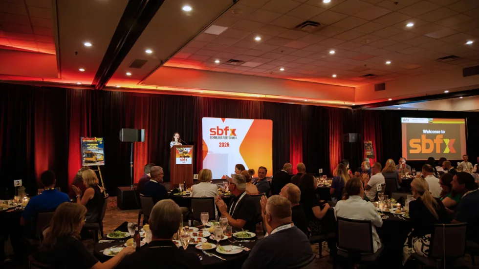 Attendees seated at banquet tables during a School Bus Fleet ConneX 2026 event, with a speaker at the podium and SBFX signage onstage.