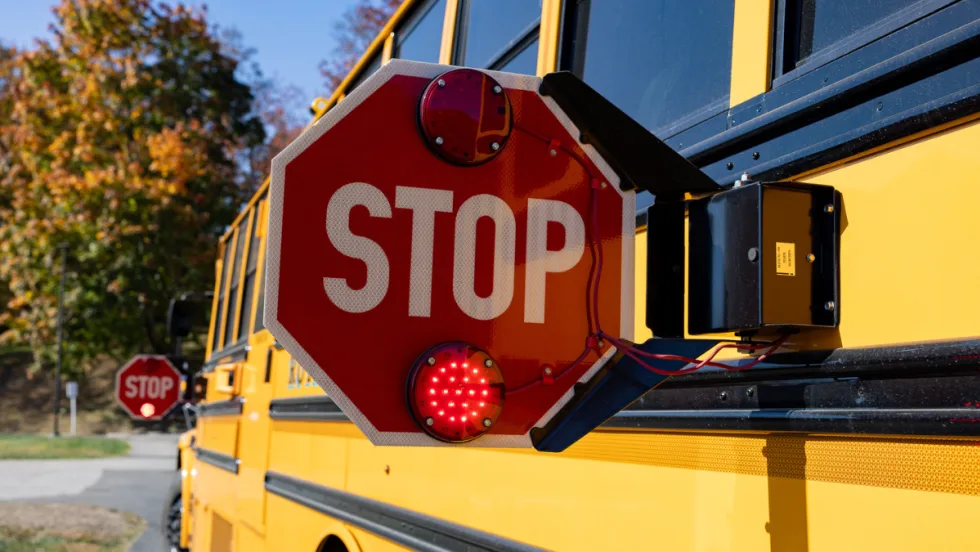 Close-up of an extended red stop arm with flashing lights on the side of a yellow school bus.
