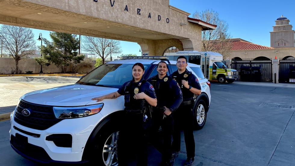 Three officers pose in front of a cruiser and sign that says Alvarado.