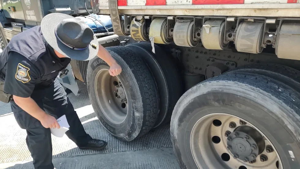 Georgia state trooper inspecting the tires on a tractor-trailer at a weigh station