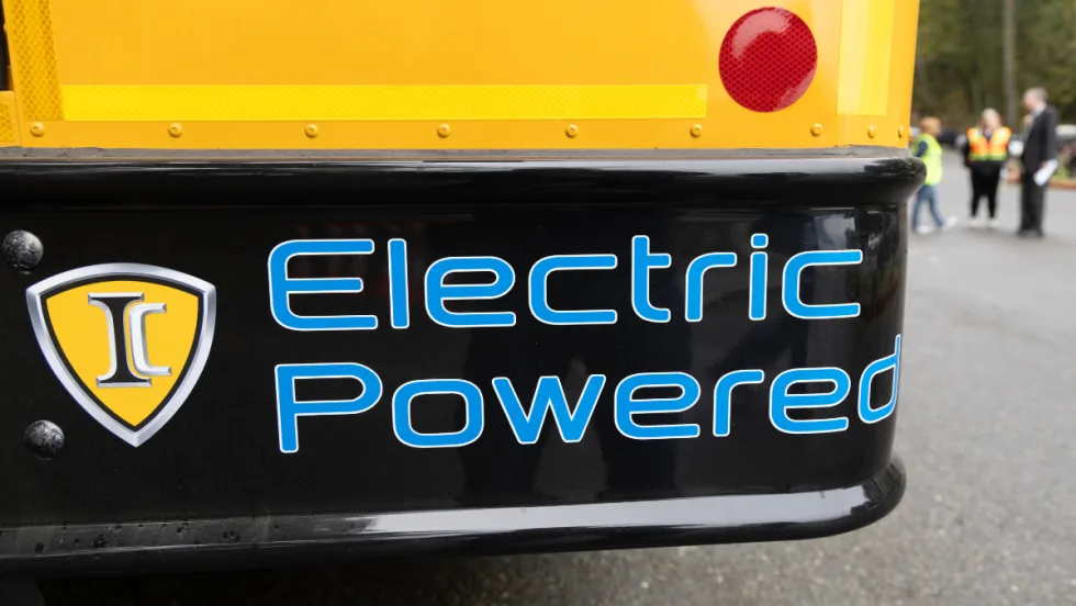 The back right corner of a school bus with blue text on the bumper reading "Electric Powered". 