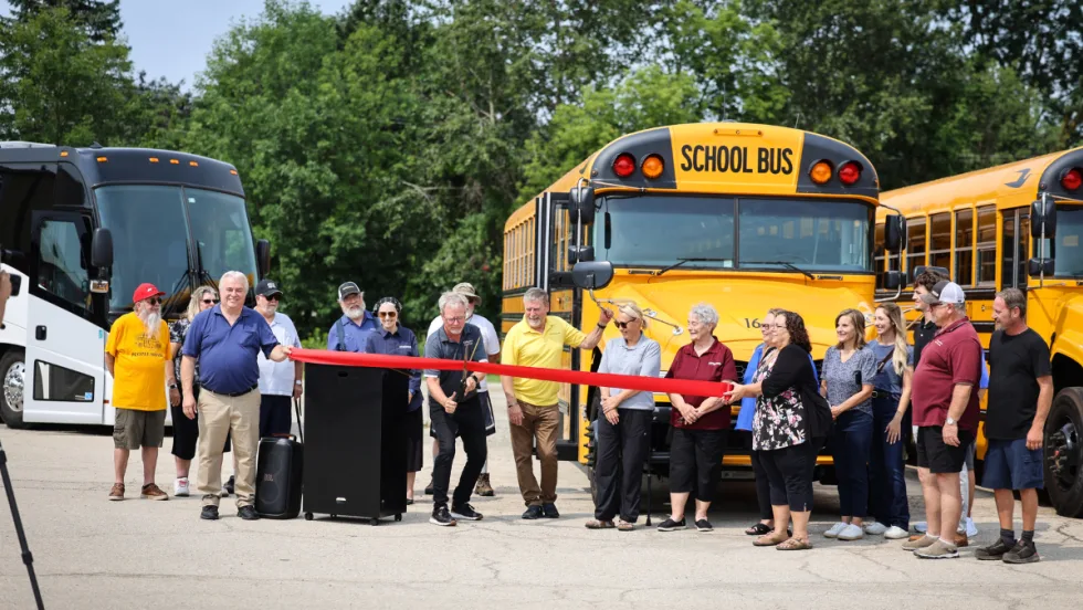 A crowd stands behind a red ribbon being cut.