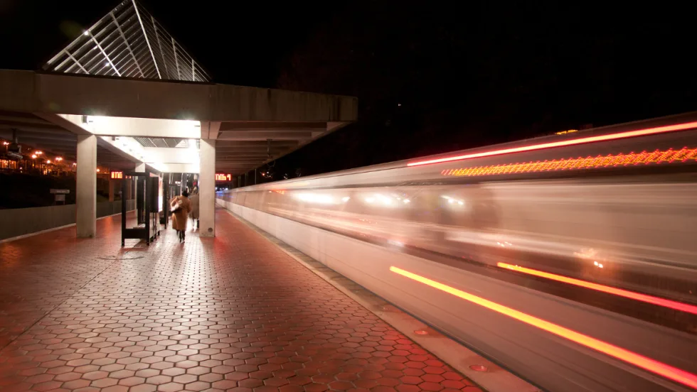 Light trails of a passenger train passing by a station at night.