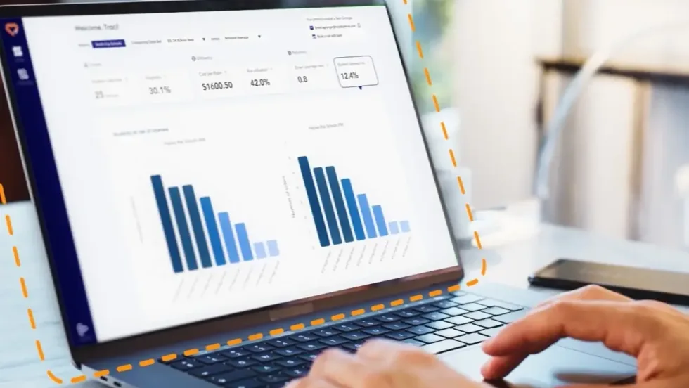 Laptop displaying HopSkipDrive RouteWise AI transportation analytics dashboard with charts and routing performance data for school district operations.