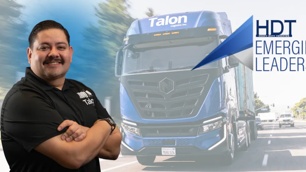 Hispanic man stands with arms crossed with electric Nikola truck in the background