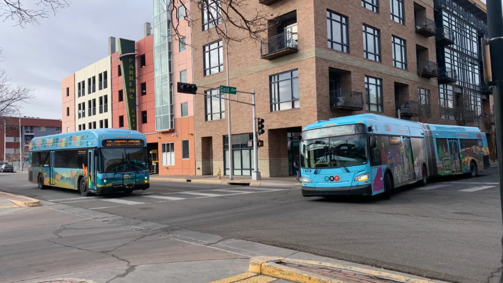 Two ABQ RIDE busses at an intersection by Gold street in front of a parking structure.