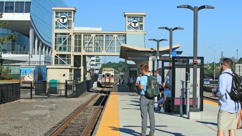 Commuter rail riders wait on a station platform.