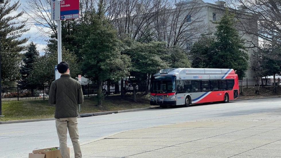 A rider waits for a WMATA bus on a sidewalk.