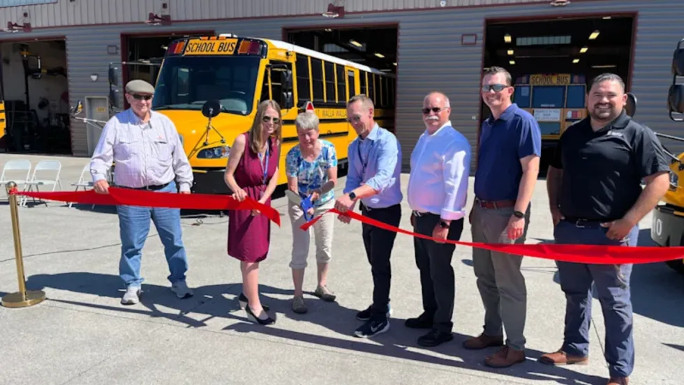 School officials cutting a red ribbon in front of electric school buses.