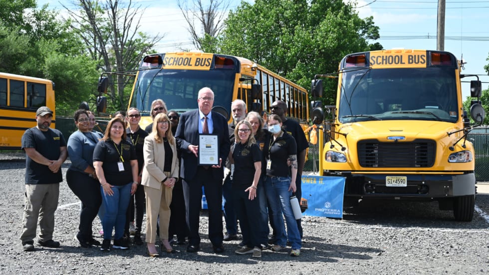 A group poses with two Thomas Built Buses Safe-T-Liner C2 Jouley electric school buses parked outside.