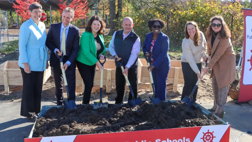 A group of people stand with shovels in dirt.
