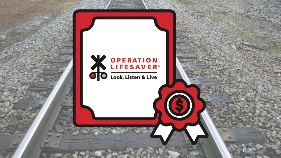 Operation Lifesaver rail safety grant graphic displayed over railroad tracks, highlighting federal funding for crossing safety and trespass prevention campaigns.