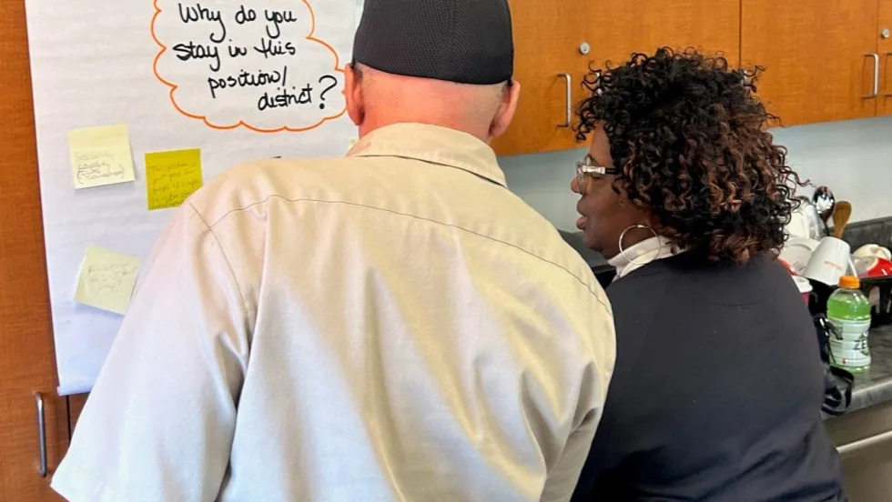 two people stand in front of a poster that says "why do you stay in this position?"