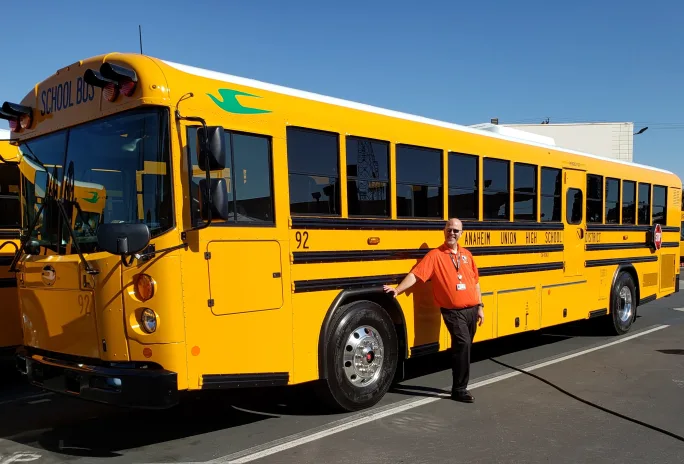 A Type D Blue Bird bus with a man posing in front of it.