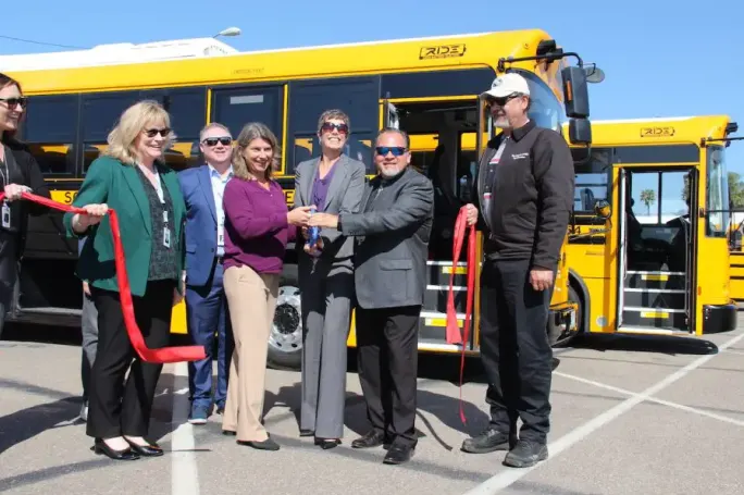 A group of people cut a ribbon in front of school buses.