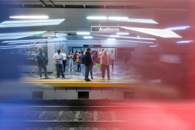 Rail patrons standing on a platform with red and blue colors in the foreground.