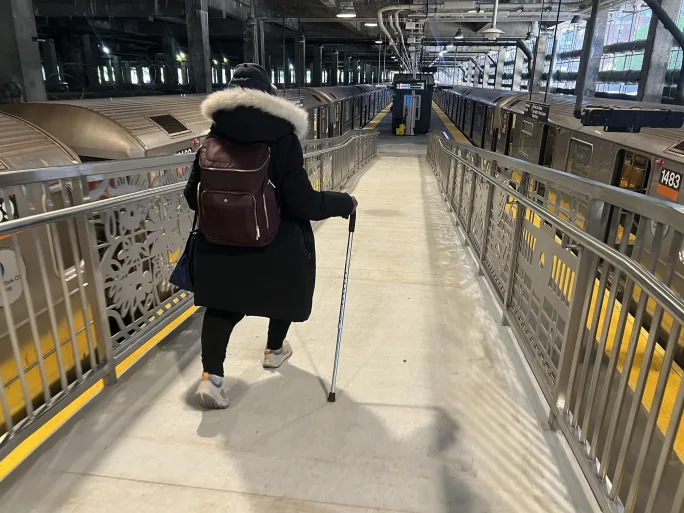 A woman with a cane walks down the new Harlem-148 Street 3 Station accessibility ramp.