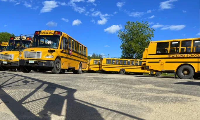 Buses in a gated yard during a sunny day.