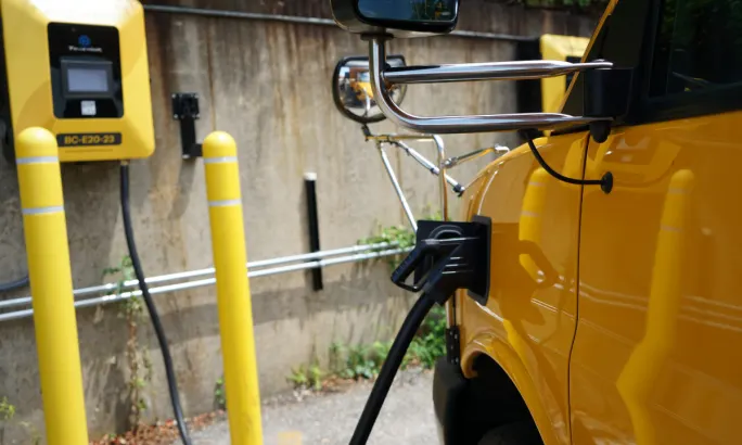 An electric school bus charges in a parking lot.