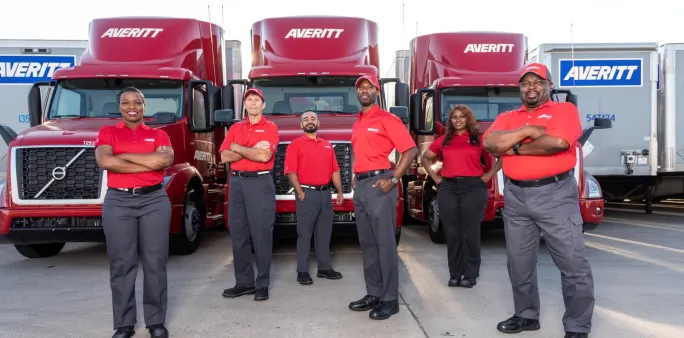Group of people in red Averitt shirts stand in front of a group of red Averitt trucks