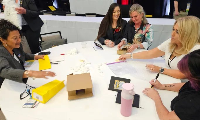Small group of attendees participate in a hands-on workshop activity at a round table, using materials for an interactive learning exercise.