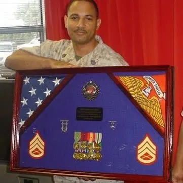 An image of a man in military fatigues holding a framed picture with military medals.