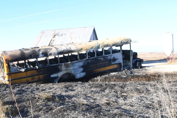 A heavily fire-damaged school bus sits beside a rural road following a bus fire in Iowa.