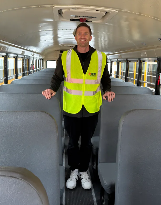 a man stands in the aisle of a school bus wearing a yellow safety vest