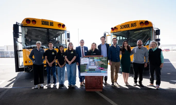 A group of people pose in front of two school buses.