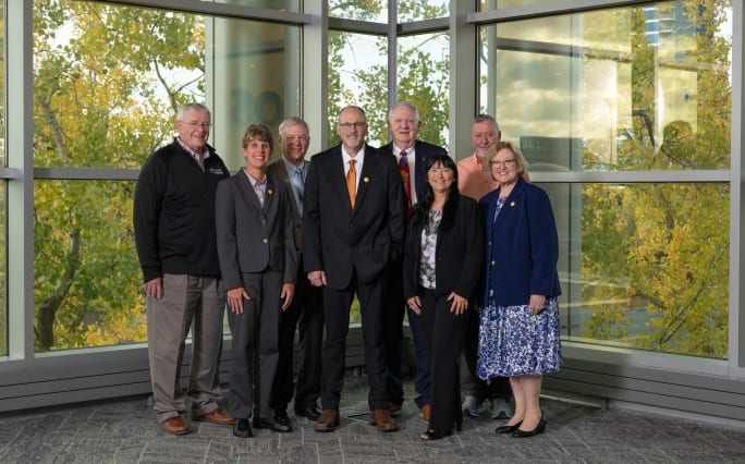 Eight NAPT Foundation board members pose for a group photo inside a building with large windows and autumn trees visible outside.