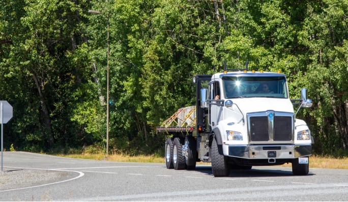 A white Kenworth T880e electric truck with flatbed body on the test track at the Paccar Technical Center.