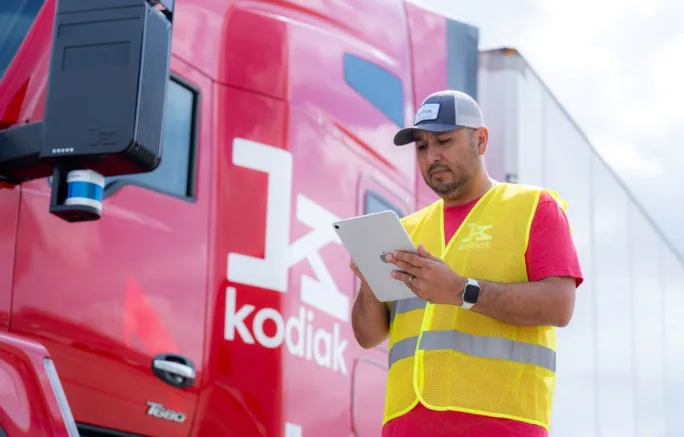 Man in yellow safety jacket with clipboard next to red Kodiak truck
