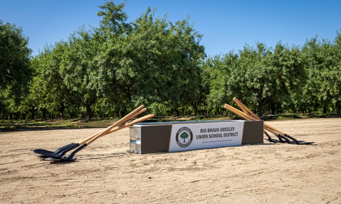 A ground breaking set up with shovels leaning on a box filled with dirt.