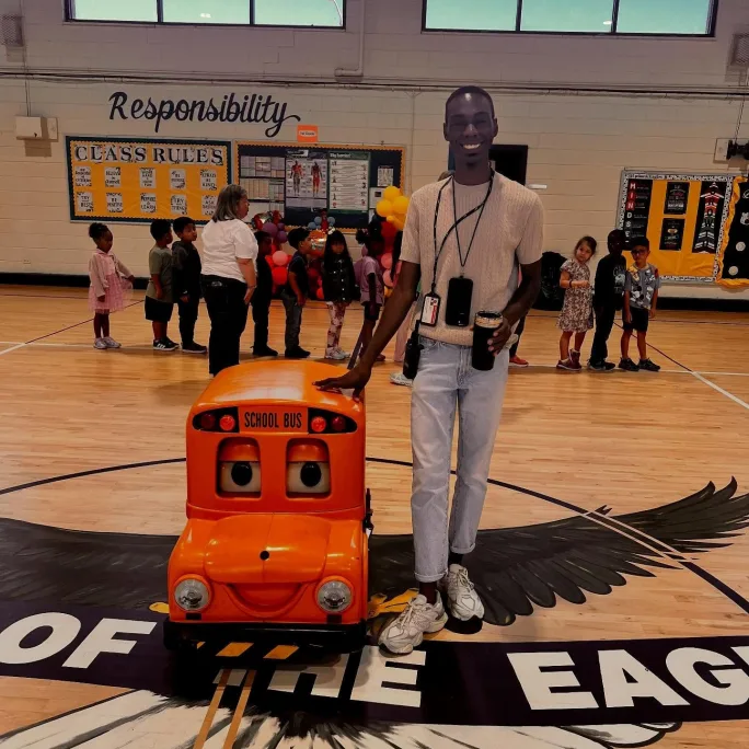 Montavia stands next to a toy school bus inside a gymnasium