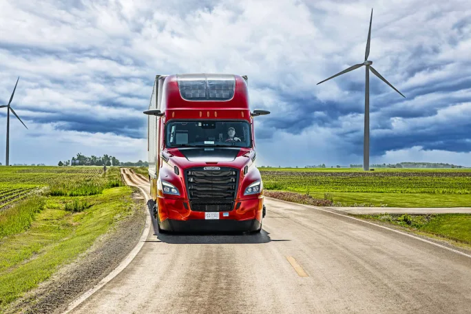 Red Nussbaum tractor going down highway with wind turbines in background