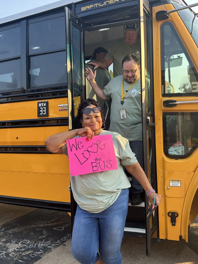 School transportation employees disembark a bus holding a pink sign that says 