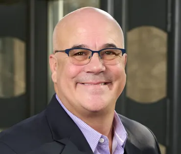 a headshot of a bald man in a black suit