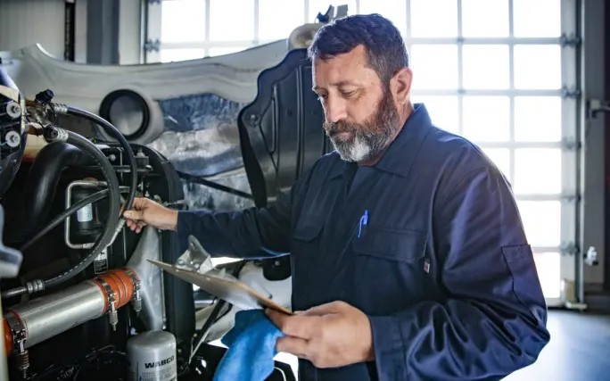 Heavy duty truck diesel technician with a checklist looking over a used truck in the shop