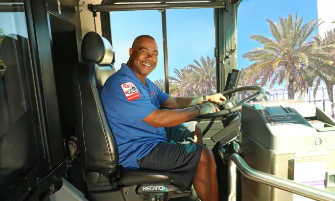 A San Diego Metropolitan Transit System bus operator smiles while seated behind the wheel of an MTS bus.