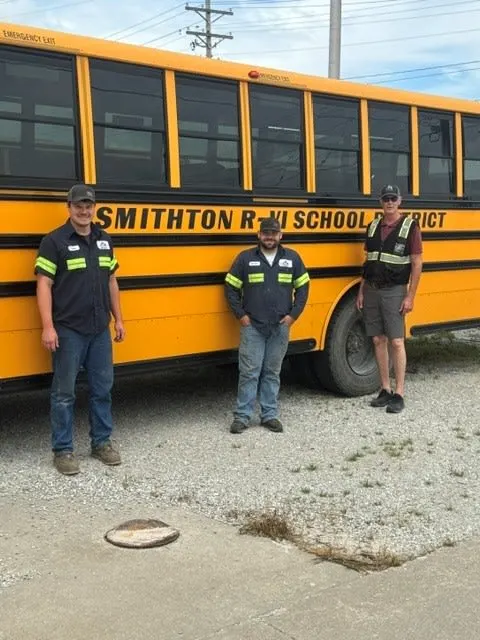 A Durham School Services bus with three people posing in front of it.