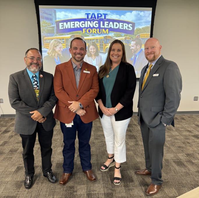 Four TAPT instructors stand together in front of a presentation screen displaying the TAPT Emerging Leaders Forum logo during the leadership development event in Texas.