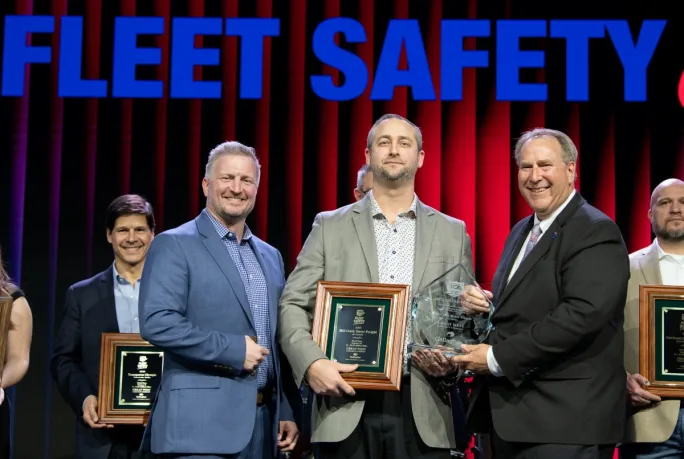 Three men in suits holding a large award plaque in front of a banner that says