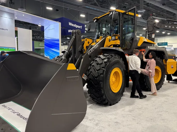 Yellow Volvo Construction Equipment on a trade show floor with two people having a discussion beside it