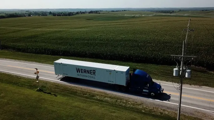 Werner tractor pulling intermodal container on highway through cropland