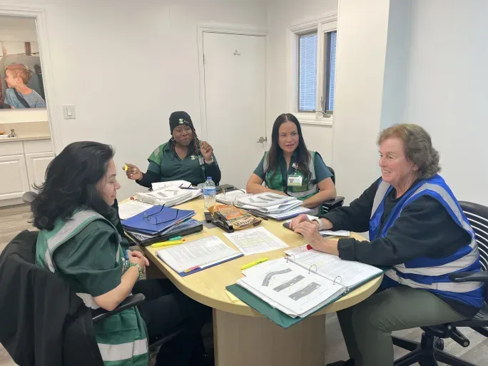 Four school transportation staff members sit around a table with training materials, binders and paperwork during a small-group driver training session.