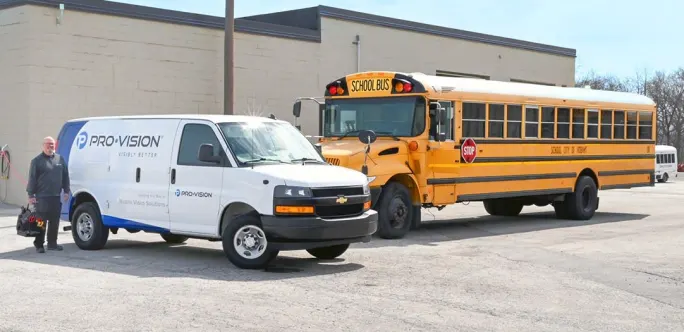 a school bus is parked next to a pro-vision van outside