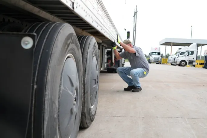 Truck driver squatting to look under trailer during a pre-trip inspection.