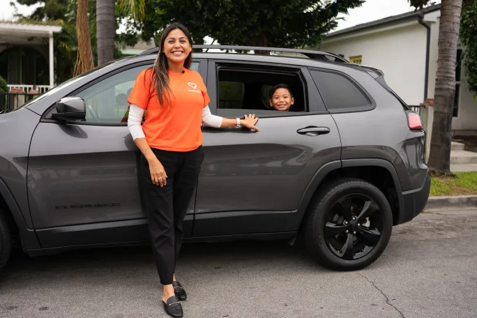 a woman stands in front of a car with a child inside