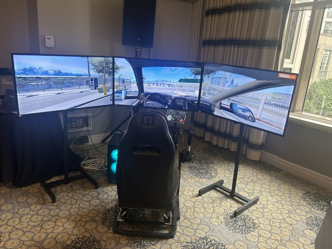 Photo of a driver's seat in front of three flat screens showing driver simulation